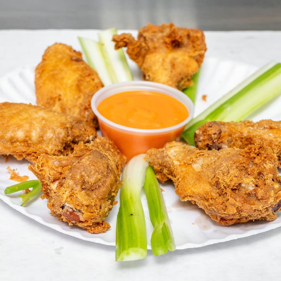 Crispy fried chicken pieces with celery sticks and a cup of orange dipping sauce on a white plate.