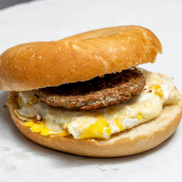 A sausage, egg, and cheese breakfast sandwich on a plain bagel, on a white surface.